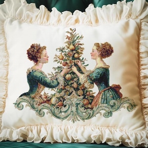 May include: Cream cushion with a frilled edge. The central design is a cross-stitch image of two women in teal dresses decorating a Christmas tree. The tree is decorated with fruit. The cushion is a square shape.
