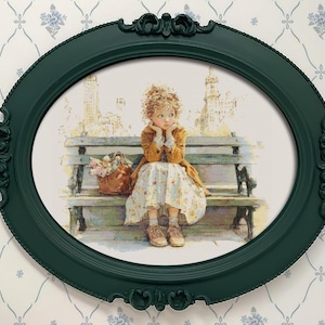 May include: An oval, dark green picture frame with ornate detailing surrounds a print of a young person sitting on a park bench. The person is wearing a yellow coat and floral dress, with a basket of flowers nearby. The background shows a cityscape.