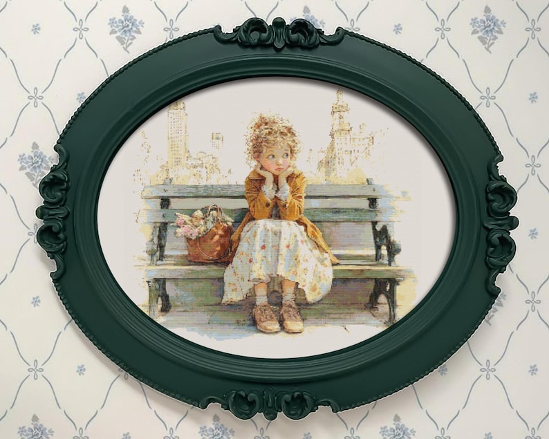 May include: An oval, dark green picture frame with ornate detailing surrounds a print of a young person sitting on a park bench. The person is wearing a yellow coat and floral dress, with a basket of flowers nearby. The background shows a cityscape.