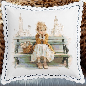 以下が含まれることがあります： 白の正方形クッション、ネイビーブルーのスカラップエッジ。公園のベンチに座る人物の水彩画イラストが描かれ、背景には都市の風景が描かれています。人物は黄色のコートと花柄のドレスを着ています。クッションは装飾品です。