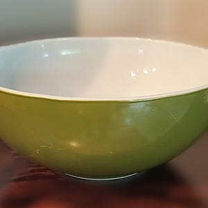 Może przedstawiać: Zielona i biała miska do mieszania o zaokrąglonym kształcie i dwóch uchwytach. Zewnętrzna strona jest błyszcząco zielona, ​​a wnętrze białe. Ten artykuł kuchenny jest przeznaczony do mieszania składników.