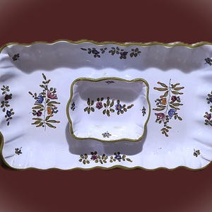 May include: A rectangular white ceramic serving tray with a scalloped edge and a green rim, featuring a smaller matching rectangular bowl in the center. Both pieces are decorated with hand-painted floral sprigs in blue, yellow, and purple.
