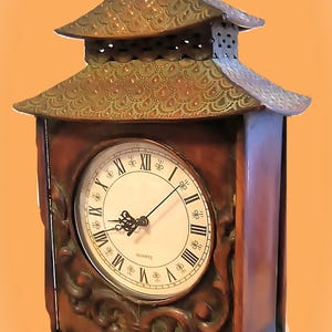 May include: A wooden quartz clock with a pagoda-style design. The clock features a white face with black Roman numerals and ornate scrollwork. The clock's roof and finial are made of a copper-colored metal.