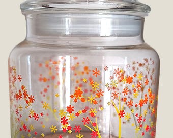 Recipiente de almacenamiento de vidrio transparente con un pequeño diseño floral naranja.