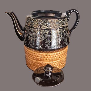May include: A black teapot with gold floral designs and a woven wicker base. The teapot has a matching lid with a knob.