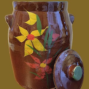 May include: A brown ceramic jar with a lid, adorned with hand-painted flowers in yellow, red, and green. The jar has two small handles and a glossy finish. The lid is placed beside the jar.