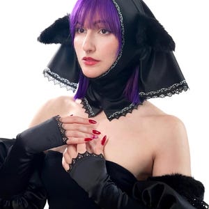 Peut inclure: Capuche noire avec des accents de fausse fourrure et une bordure en dentelle. La capuche a des formes en forme d'oreilles et un col assorti. Le modèle porte des gants sans doigts noirs avec une bordure en dentelle. Logo Red Lily en bas à gauche.