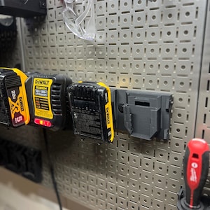 May include: A gray metal pegboard with various tools and accessories. Includes yellow and black DeWalt 20V lithium-ion batteries, a black battery holder, safety glasses, and a red and black screwdriver. The pegboard has a grid pattern.