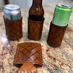 May include: A set of handcrafted brown leather drink holders and a matching coaster. The holders feature a diamond pattern and are designed to hold a beer bottle and cans. The coaster has the initials "C.B." embossed on it.