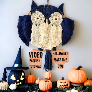 Op de afbeelding: Een macram&eacute; uil wanddecoratie met marineblauwe vleugels en een cr&egrave;mekleurig lichaam. De uil is versierd met houten kralen en een houten deuvel. De afbeelding bevat ook een zwarte pompoen met een heksenhoed en verschillende oranje pompoenen. Tekst op het bord luidt "VIDEO PATTERN TUTORIAL" en "HALLOWEEN MACRAME OWL".
