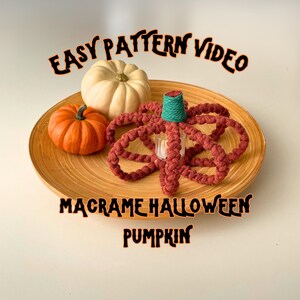 Pode incluir: Uma abóbora de macramé vermelha com uma parte superior turquesa, cercada por duas abóboras reais em um prato de madeira. O texto "Easy Pattern Video" está na parte superior da imagem e "Macrame Halloween Pumpkin" está na parte inferior.