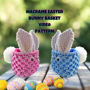 May include: Two macrame bunny baskets, one pink and one blue, with white pom-poms for tails. The baskets are filled with colourful Easter eggs. The image includes the text "Macrame Easter Bunny Basket Video Pattern".