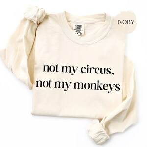 Könnte beinhalten: Elfenbeinfarbenes Langarmshirt mit dem schwarzen Text "not my circus, not my monkeys". Das Shirt hat einen Rundhalsausschnitt und ein Etikett mit der Aufschrift "Comfort Colors".