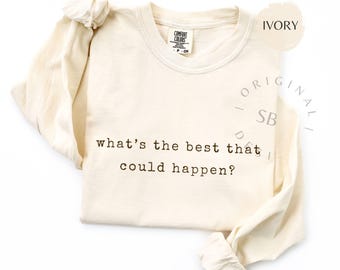 Könnte beinhalten: Elfenbeinfarbenes Langarmshirt mit dem Text "what's the best that could happen?" in Dunkelbraun. Das Shirt hat einen Rundhalsausschnitt und ein Etikett mit der Aufschrift "Comfort Colors".