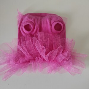 Peut inclure: Un pull rose vif pour chien, avec une texture c&ocirc;tel&eacute;e et des ouvertures pour les pattes avant. Il est orn&eacute; d'une jupe en tulle rose scintillante superpos&eacute;e, cr&eacute;ant un effet tutu. Le v&ecirc;tement est con&ccedil;u pour un petit chien.