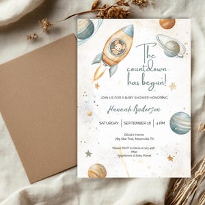 Op de afbeelding: Baby shower uitnodiging met een ruimtethema. De uitnodiging toont een raket met een muis, planeten en de tekst "De aftelling is begonnen!" Bevat details voor Hannah Andersons babyshower.