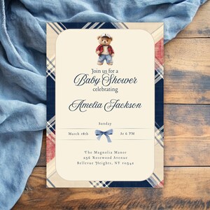 May include: A baby shower invitation with a blue and red tartan pattern. The invitation features a teddy bear wearing a red and blue tartan shirt and a blue baseball cap. The text on the invitation reads "Join us for a Baby Shower celebrating Amelia Jackson. Sunday, March 18th at 6 PM. The Magnolia Manor, 286 Rosewood Avenue, Bellevue Heights, NY 10549."