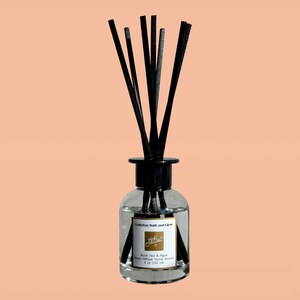 May include: A clear glass bottle with a black lid and black diffuser sticks. The bottle contains a reed diffuser with the scent "Black Tea & Figue" and the brand name "Katie Ray Bath and Glow". The bottle is labeled with "Reed Diffuser Home Aroma" and "4 oz (150 ml)".