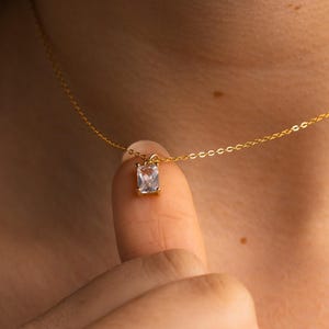 Puede incluir: Un collar de cadena de oro con un pequeño colgante rectangular transparente.