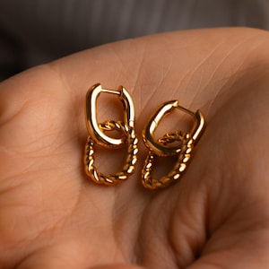 Puede incluir: Un par de pendientes de aro de oro con un diseño trenzado. Los pendientes están hechos de dos aros, uno más grande que el otro, que están conectados entre sí.