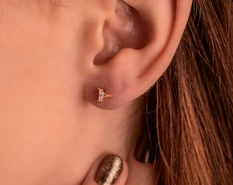 May include: A close-up of a person's ear with a small gold triangle earring with a clear stone in the center.