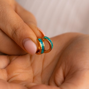 Könnte beinhalten: Ein Paar goldene Creolen mit türkisfarbenem Inlay. Die Ohrringe sind klein und zart.