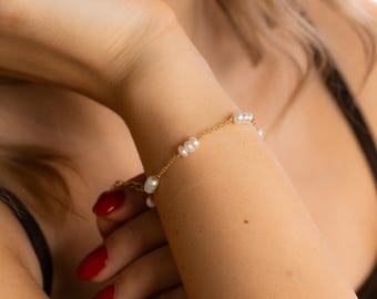 Op de afbeelding: Een delicate gouden kettingarmband met kleine witte parels. De armband zit om een pols.