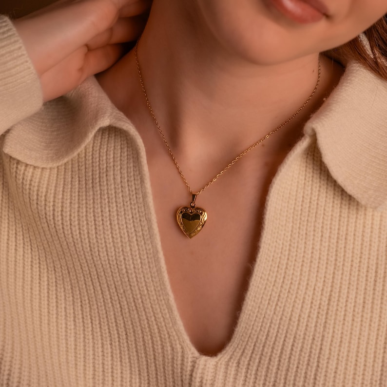 May include: A gold heart-shaped locket necklace on a person wearing a cream-colored sweater.
