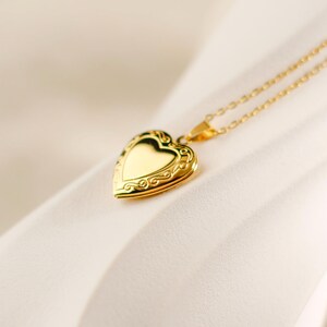 May include: A gold heart-shaped locket necklace with a delicate chain. The locket has an ornate design and is perfect for holding a small photo or memento.