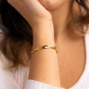 May include: A gold-toned braided chain bracelet. The bracelet is made of a woven metal design.