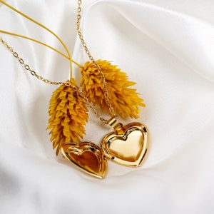 May include: Two gold heart-shaped locket necklaces with delicate chains. The lockets are open and the chains are draped over dried yellow flowers.