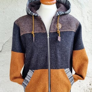 May include: A color-blocked zip-up hoodie featuring a brown upper chest, a dark charcoal gray midsection, and a mustard yellow lower section and sleeves. The hood is lined with a black and white patterned fabric, and the pockets feature matching trim.