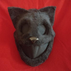 May include: Black plush cat mask with black felt eyes and nose. The mask has a wide, open mouth.
