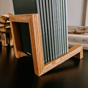 Może przedstawiać: Drewniany stojak na książki z kolekcją ciemnozielonych dzienników. Dzienniki są oznaczone miesiącami roku, w tym "Listopad 2021" i "Październik 2021". Stojak jest wykonany z jasnego drewna.