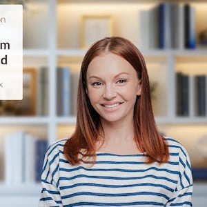 May include: A woman with long, red hair smiles at the camera. She is wearing a striped blue and white shirt. The background is a blurry image of a bookshelf with books and decorative objects.