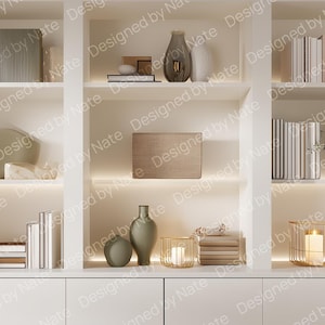 Könnte beinhalten: Ein weißer Einbauschrank mit mehreren Regalen, gefüllt mit Büchern, Vasen, Kerzen und dekorativen Objekten. Die Regale sind mit warmer Beleuchtung versehen, was eine gemütliche und einladende Atmosphäre schafft. Der Text "Designed by Nate" ist sichtbar.