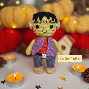 Könnte beinhalten: Handgemachte Häkelpuppe von Frankenstein mit grünem Gesicht, schwarzen Haaren und grauen Ohren. Die Puppe trägt ein orangefarbenes Hemd, eine lila Weste und eine blaue Hose. Der Text "Crochet Pattern" ist sichtbar. Der Hintergrund umfasst Kürbisse und brennende Kerzen.