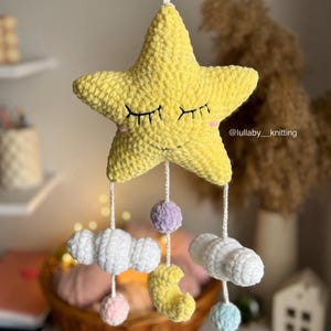 May include: A handmade yellow star mobile with closed eyes, clouds, moon, and pom-poms. The star is the central element, with dangling clouds, a crescent moon, and colorful pom-poms. The mobile is designed for a nursery or baby's room.