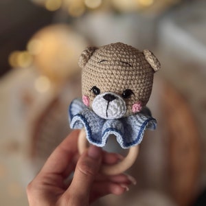 May include: A crocheted brown bear rattle with blue ruffle trim and a wooden ring.