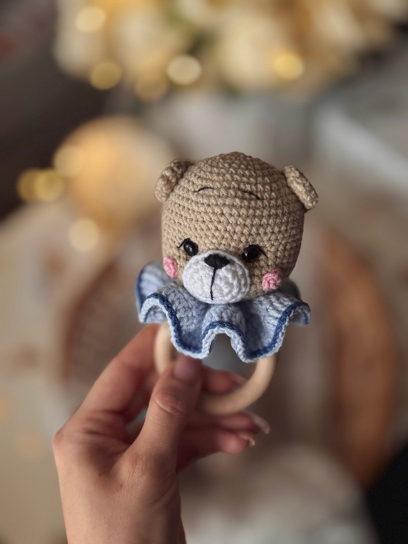 May include: A crocheted brown bear rattle with blue ruffle trim and a wooden ring.