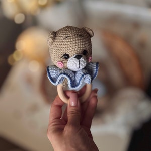 May include: A crocheted brown bear rattle with blue and white ruffle trim attached to a wooden ring.