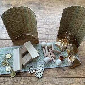 May include: An overhead shot displays a collection of craft supplies on a wooden surface. Two woven baskets flank a green and white patterned runner. Wooden blocks, dowels, and spheres are arranged alongside gold-colored pouches and decorative coins.