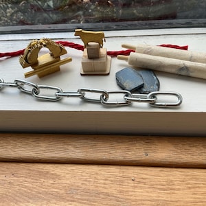 Op de afbeelding: Een verzameling religieuze voorwerpen, waaronder een gouden menorah, een houten rol, een klein houten koeienbeeldje en een ketting. De voorwerpen zijn op een wit oppervlak gerangschikt.