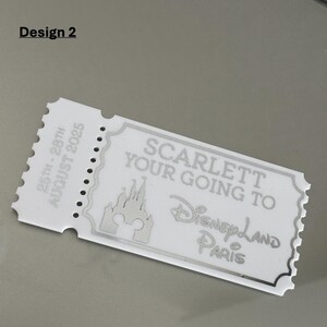 May include: A white ticket-shaped keepsake with the text "SCARLETT YOUR GOING TO Disneyland PARIS" and a castle graphic. The ticket also includes the dates "25th - 28th AUGUST 2025" and the words "Design 2".