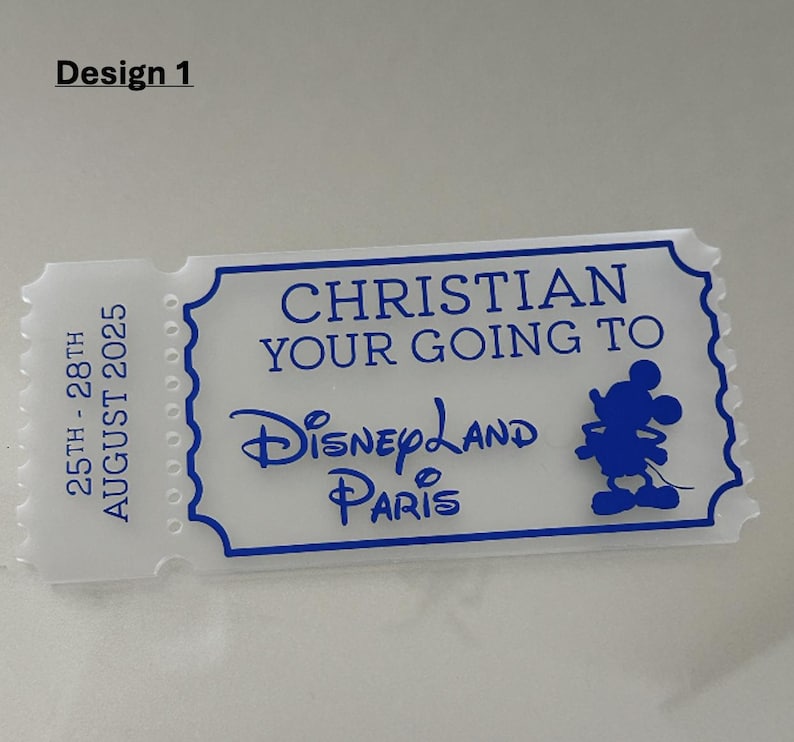 May include: A white ticket-shaped souvenir with blue text and a blue outline. The text reads "CHRISTIAN YOUR GOING TO Disneyland Paris" with a Mickey Mouse silhouette. The left side of the ticket has the dates "25TH - 28TH AUGUST 2025".