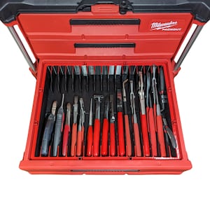 May include: Open red and black tool case with a variety of hand tools. The case is labeled "Milwaukee PACKOUT" and contains pliers, cutters, and other tools with red handles. The tools are neatly organized within the case.