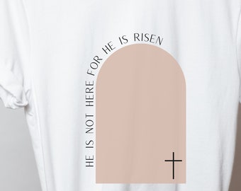 Può includere: Maglietta bianca con un arco color pesca e una croce nera. Il testo "He is not there for He is risen" è scritto attorno all'arco.