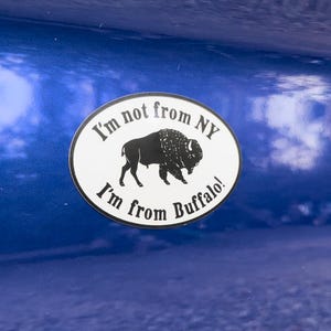 May include: A white oval sticker with black text and a black silhouette of a buffalo. The sticker reads "I'm not from NY I'm from Buffalo!"