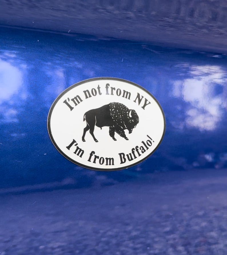May include: A white oval sticker with black text and a black silhouette of a buffalo. The sticker reads "I'm not from NY I'm from Buffalo!"