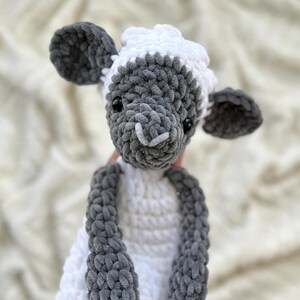 May include: A crocheted plush toy sheep with a white body and gray legs, head, and ears. The sheep has black eyes and a white nose.